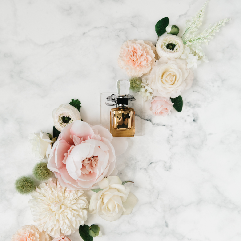 Image of fragrance bottle surrounded by flowers, on a marble table. 